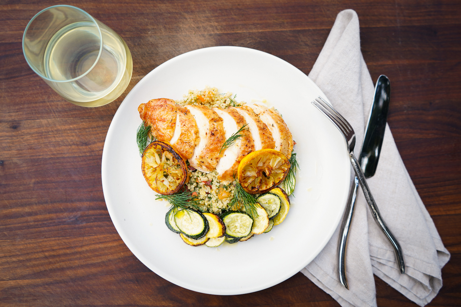 A composed dinner setting with chicken, seasonal vegetables, and wine